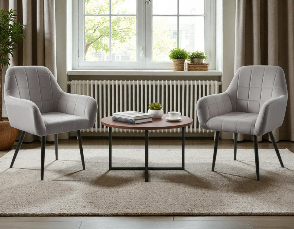 Two light grey Wilhelm armchairs with armrests in a modern room with a round coffee table and large window
